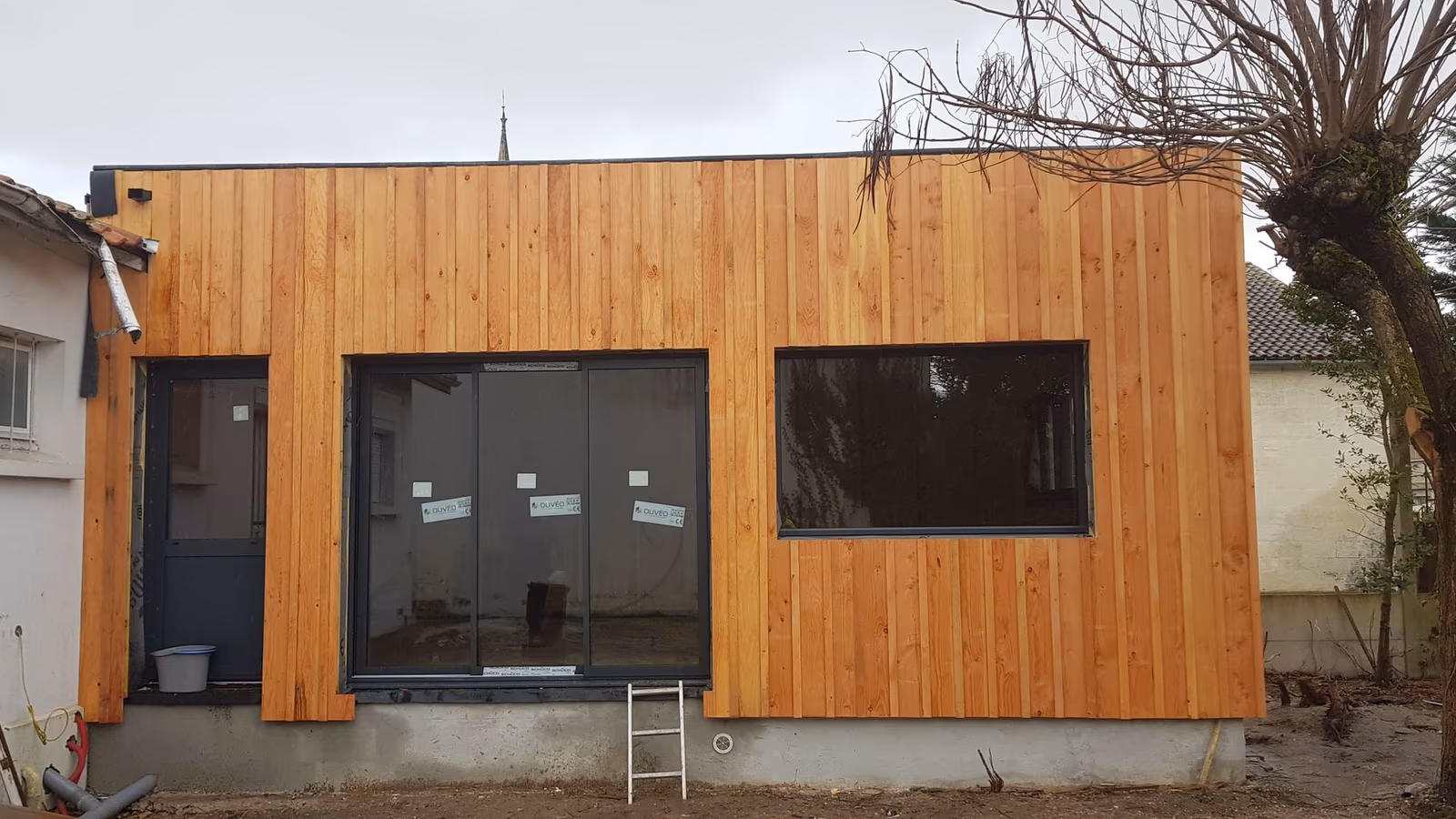 Extension à toit plat en ossature bois avec bardage bois vertical, chantier en cours à Bordeaux