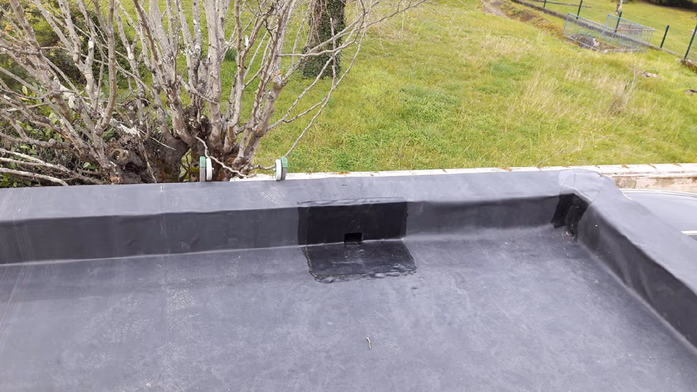 Membrane EPDM noire terminée sur un toit plat à Podensac, relevés sur acrotère et évacuation d'eau pluviale