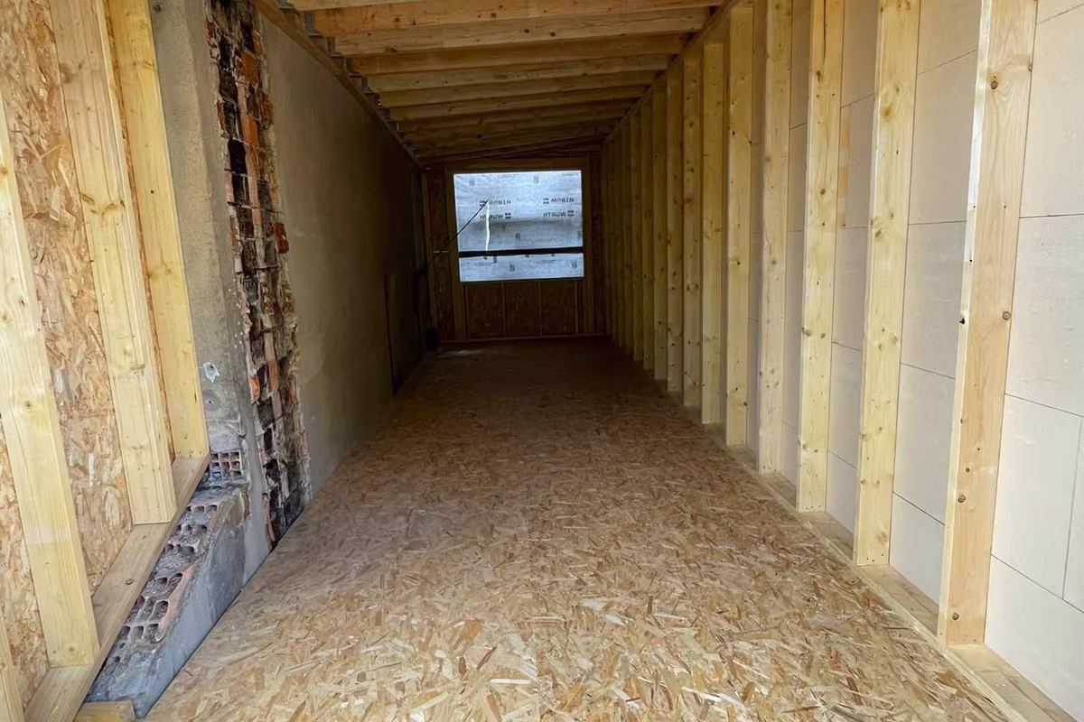 Ossature bois montée contre un mur en brique existant, plancher OSB posé et solivage apparent