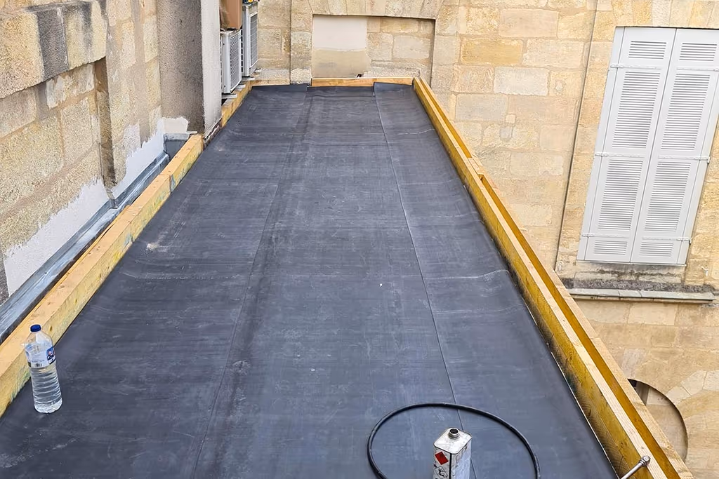 Membrane EPDM noire posée en lés sur un toit plat à Bordeaux, rives en bois contre un mur en pierre